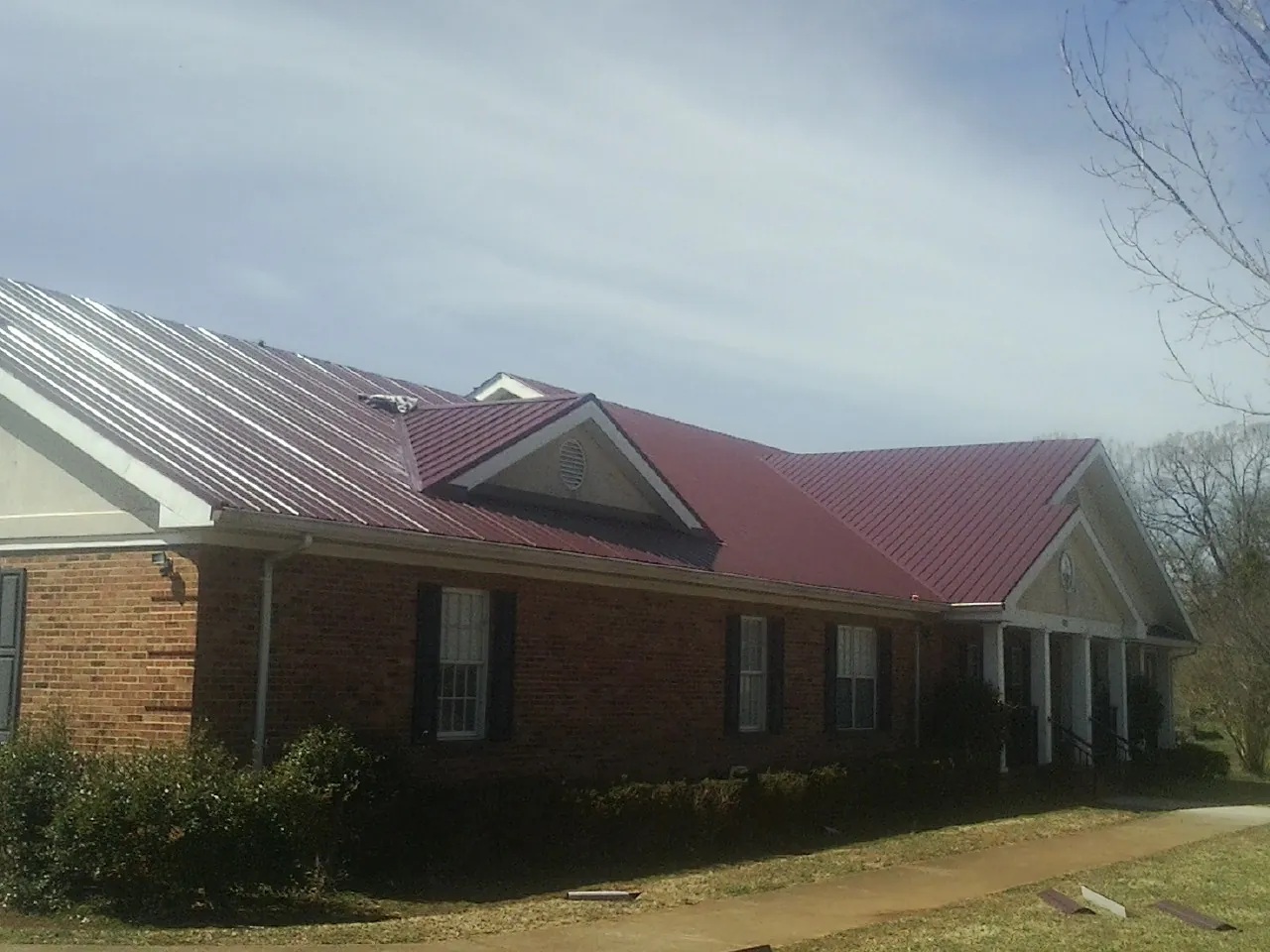 Red metal roof with gabled entries on a long brick building, from a Hail Damage Roof Repair job in Keysville