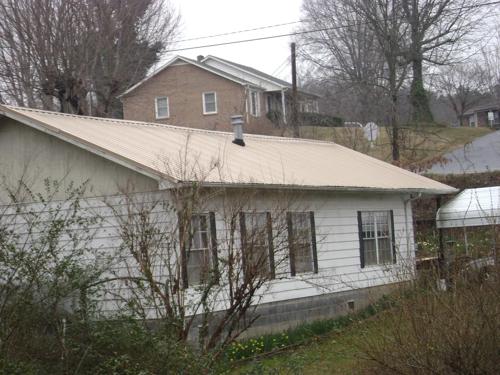 Tan metal roof on a white sided house set into a hillside — Commercial Roofing by Roofing Brothers in Keysville